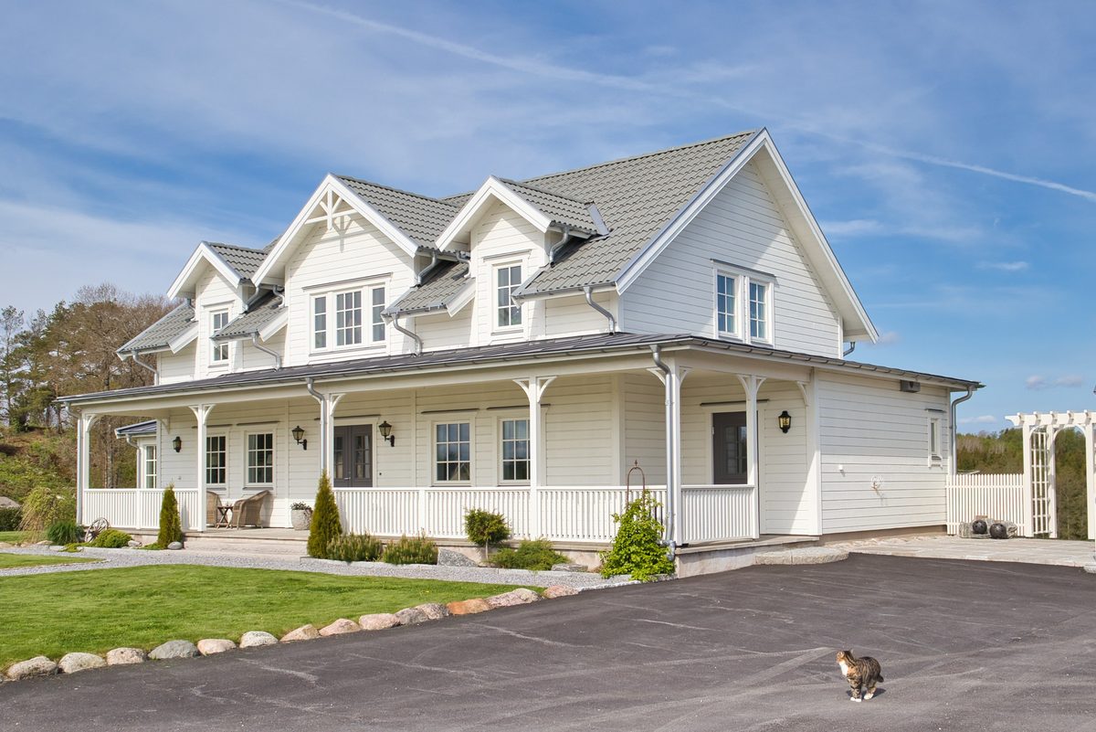 Vit villa med bred veranda och asfalterad infart