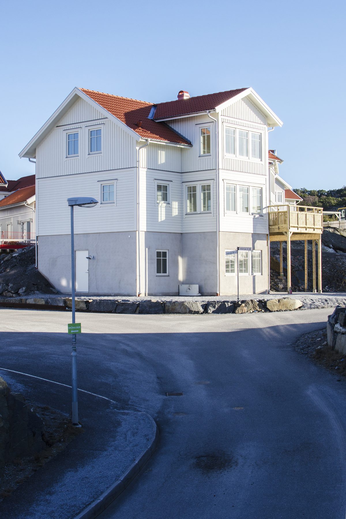 Vit kustvilla med rött tak och flera våningar sedd från gatan