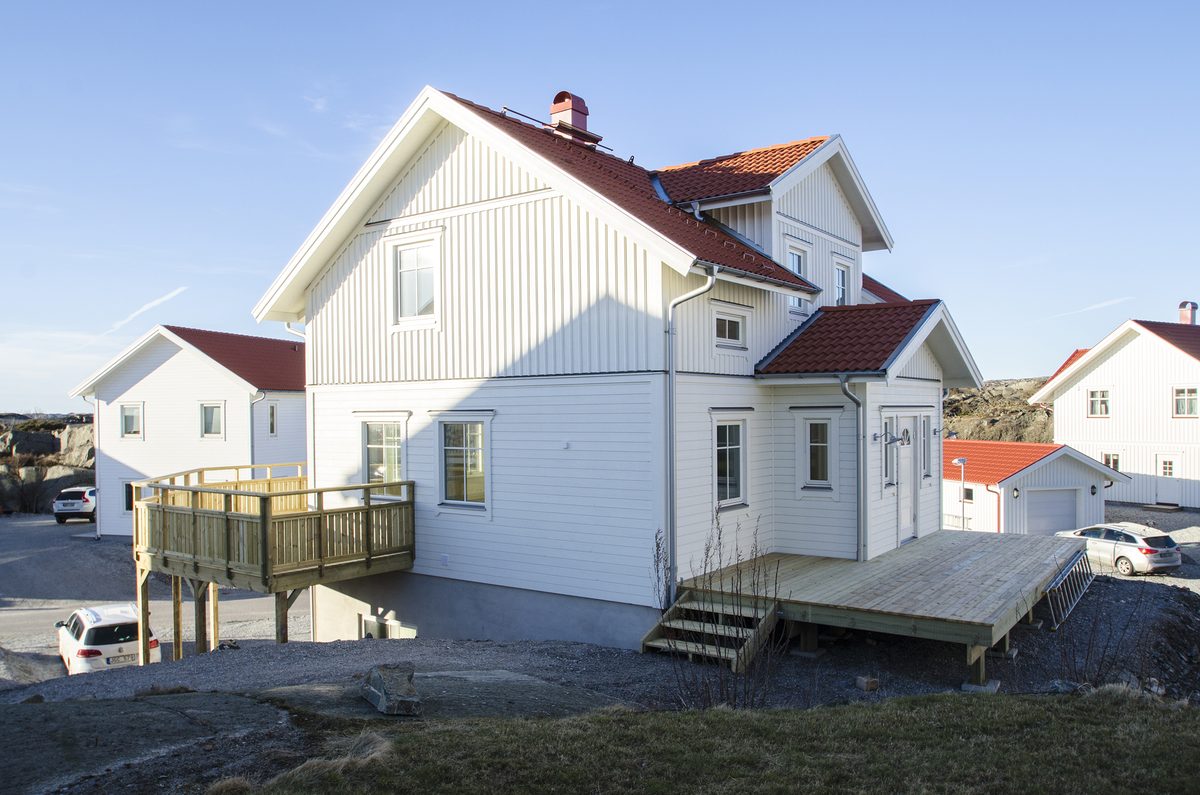 Vit träfasad med rött tak och trädäck runt husets hörn