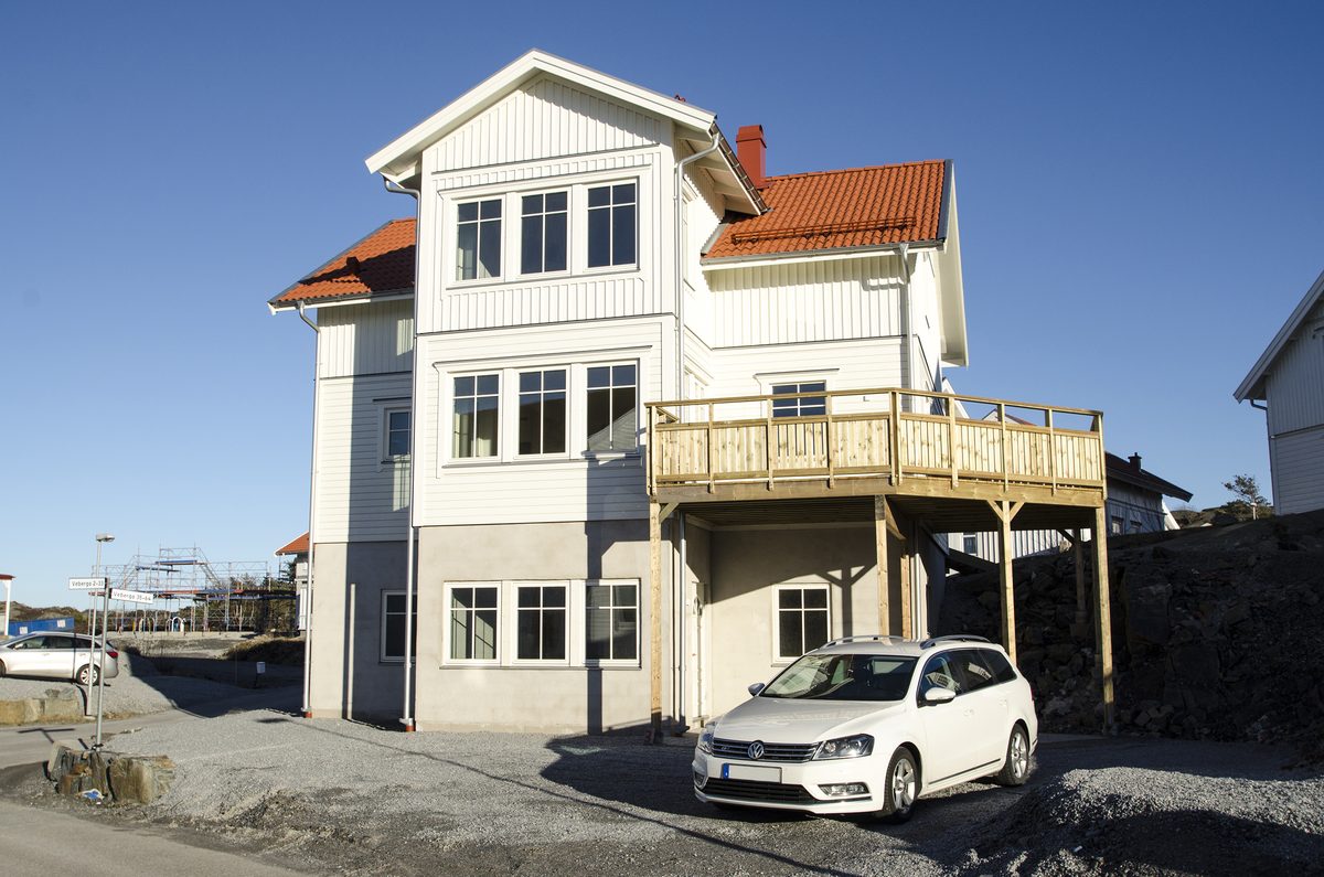 Vit villa med balkong ovanför carport och en bil på infarten