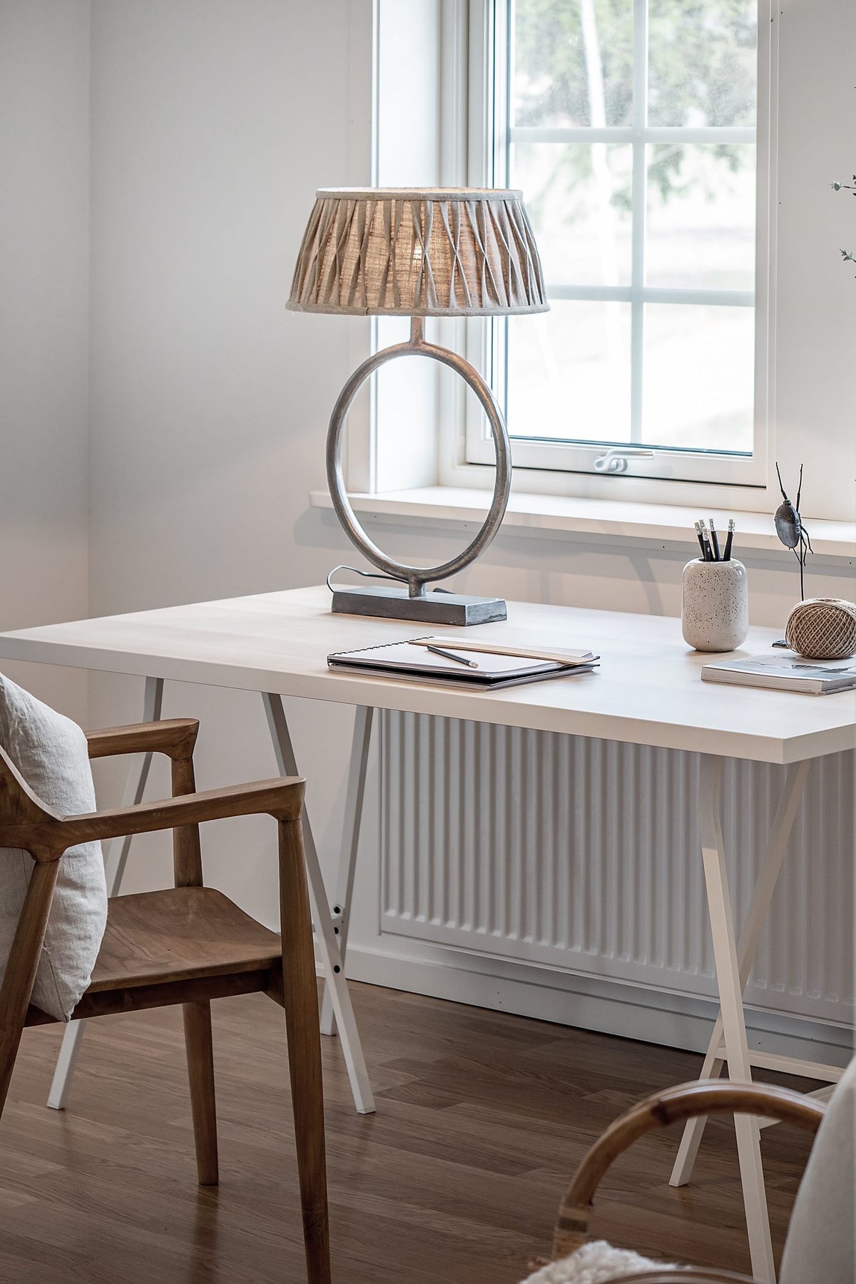 Vitt skrivbord med lampa framför ett spröjsat fönster