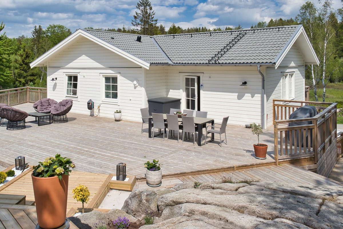Trädäck och utemöbler intill husets vita gavel och berget