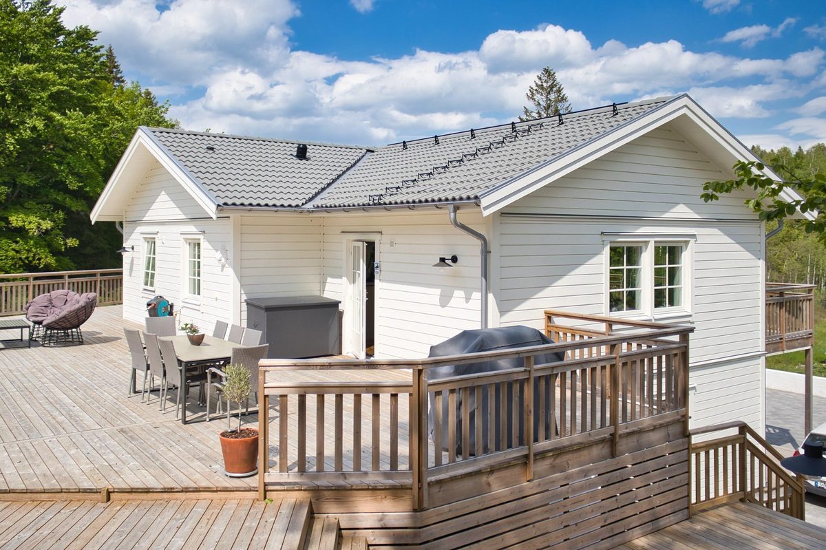 Vit träfasad med ett stort trädäck och träräcke
